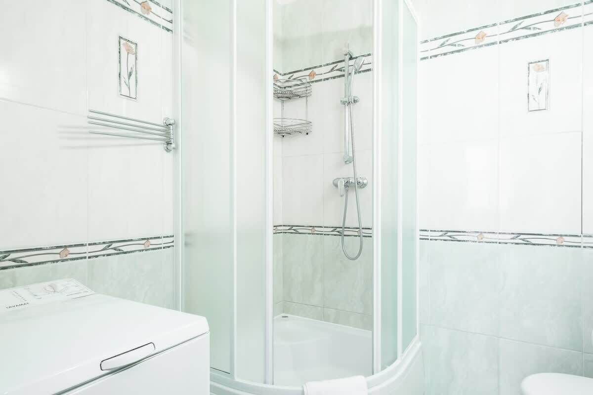 A modern bathroom with a glass-enclosed shower, white tiles, and a white toilet.