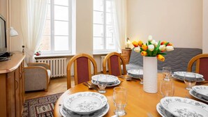 Comedor con una mesa de madera dispuesta para cuatro personas, rodeada de sillas. Hay un jarrón con flores sobre la mesa, y se aprecia un radiador al fondo.