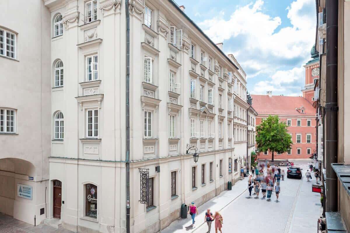 Um edifício histórico com arquitetura clássica, uma placa de museu e uma rua com pedestres.