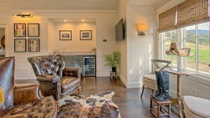 A spacious living room with leather armchairs, a dining area with a wooden table, and a large window with a view of the outdoors.