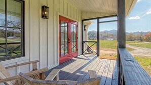 A wooden porch with a red door, a view of a rural landscape, and a clear sky.