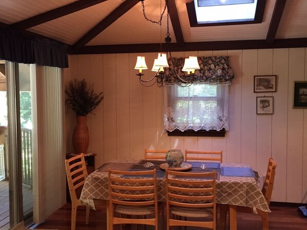 A dining area with a table set for four, wooden chairs, a chandelier, and a window with lace curtains.