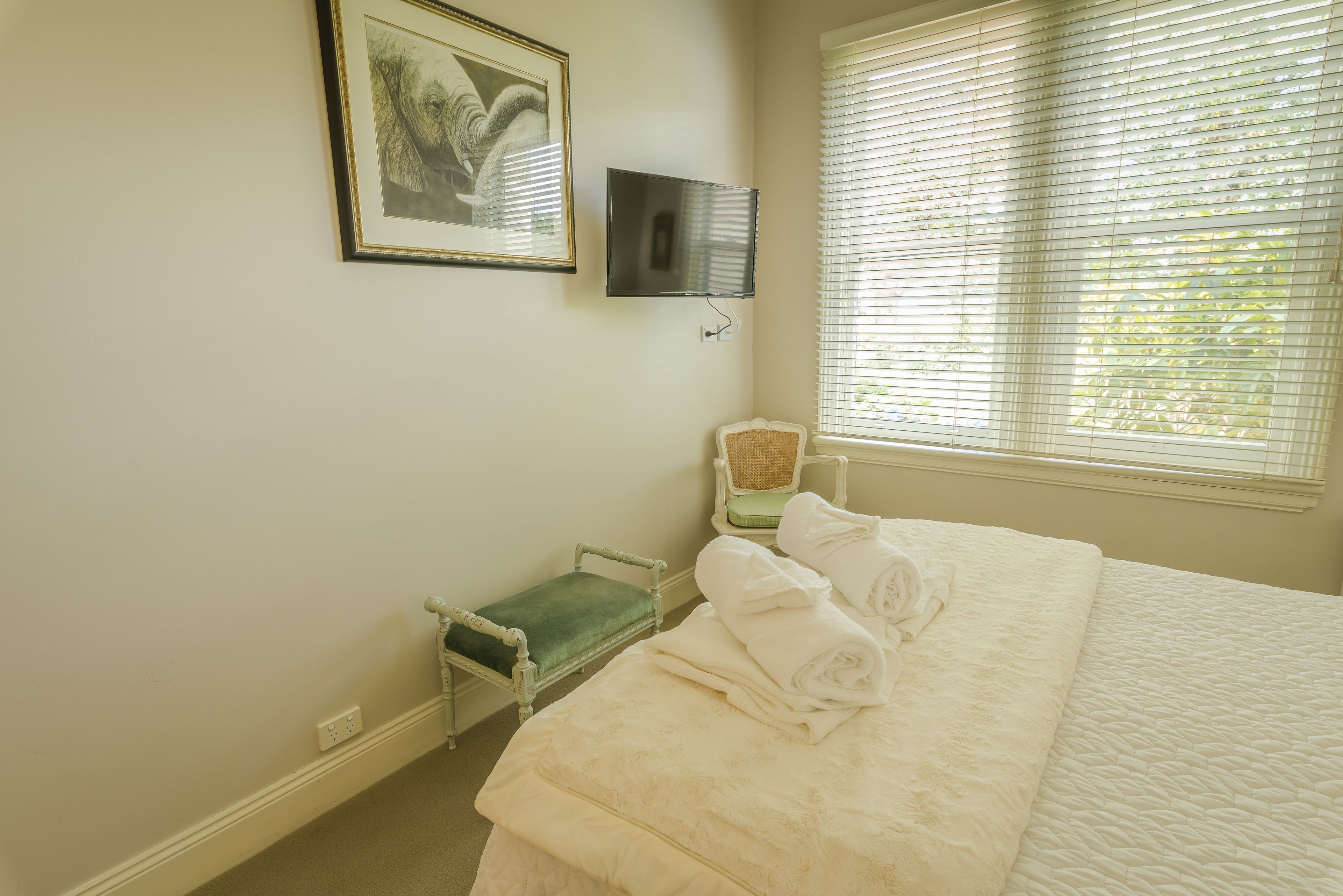 A bedroom with a bed, a chair, a small table, a framed picture, and a window with blinds.