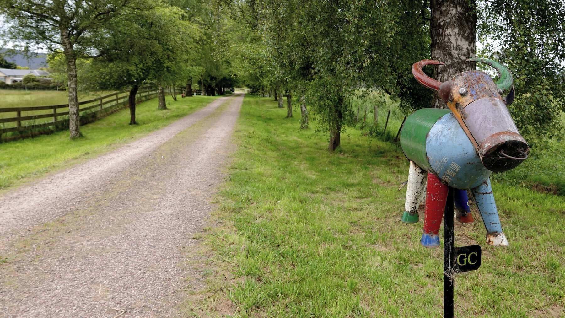 A rural road flanked by trees and a decorative metal sculpture.