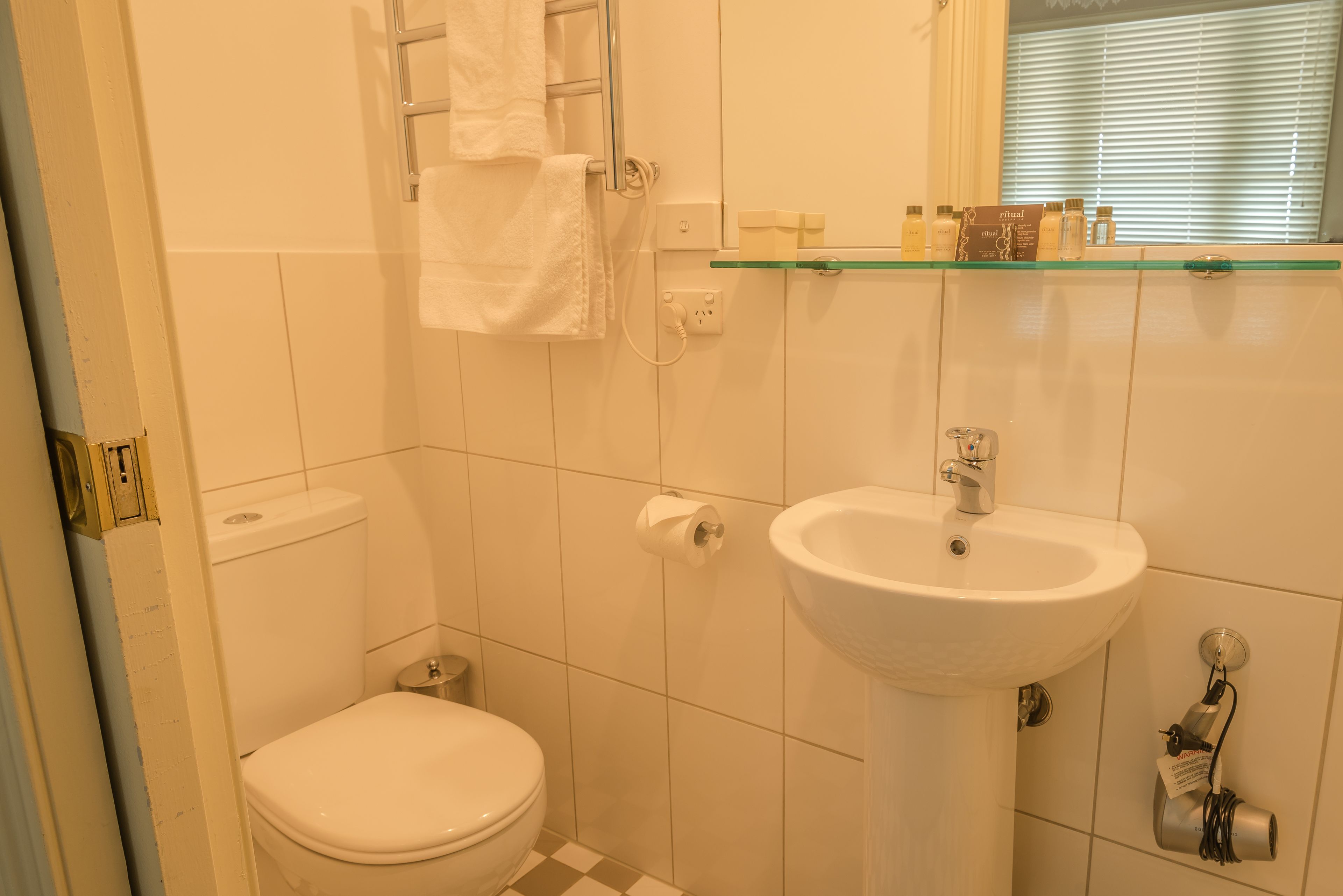 Ein Badezimmer mit Toilette, Waschbecken und einer Glasablage mit Pflegeprodukten.