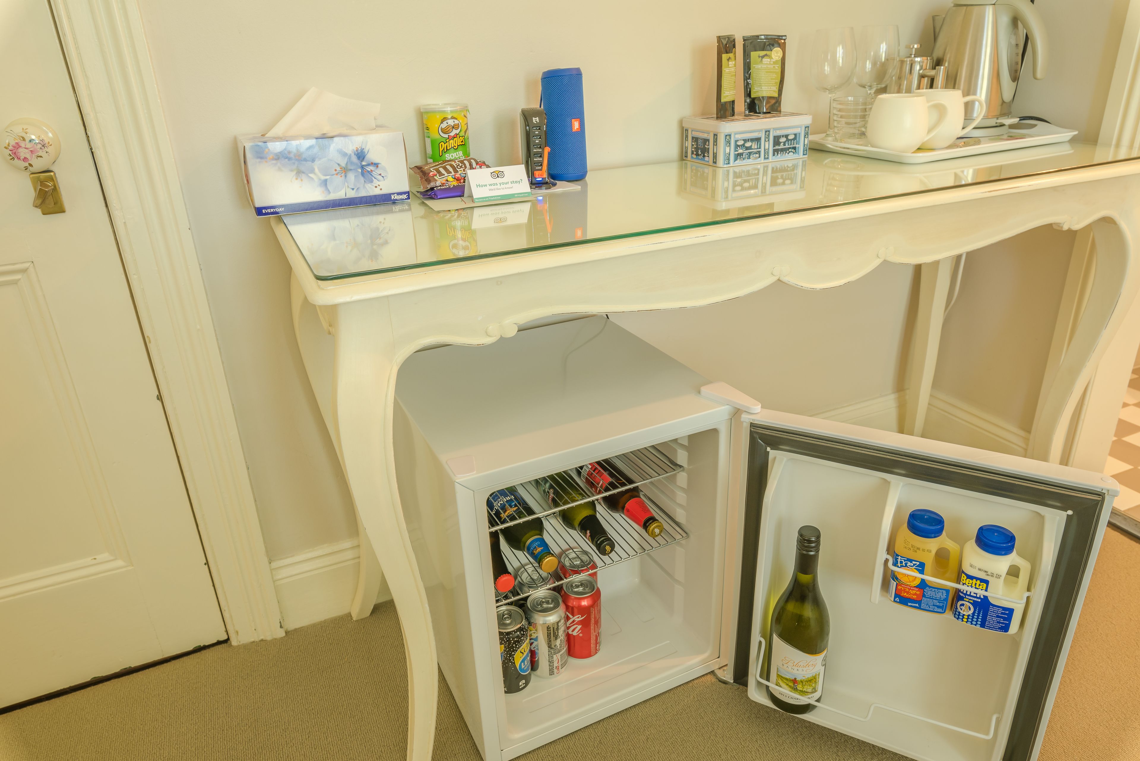 A compact refrigerator with a glass top, containing beverages and a bottle of wine.
