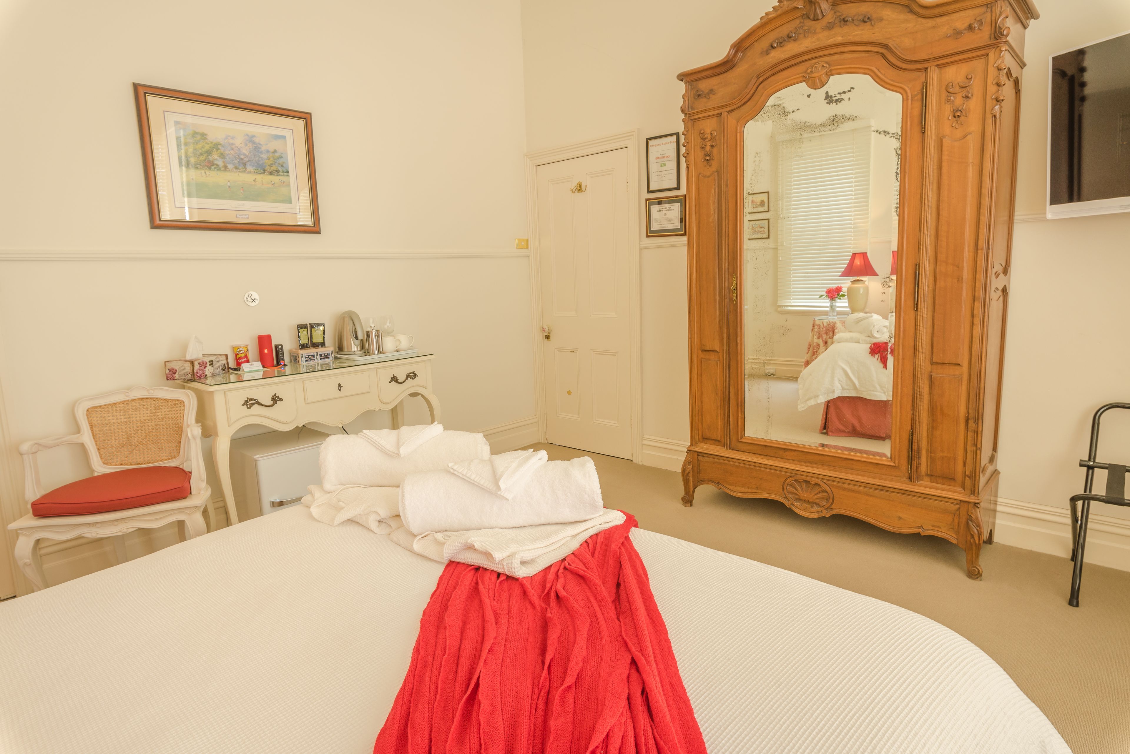 Un dormitorio con cama, armario de madera, silla, cómoda y un cuadro en la pared.