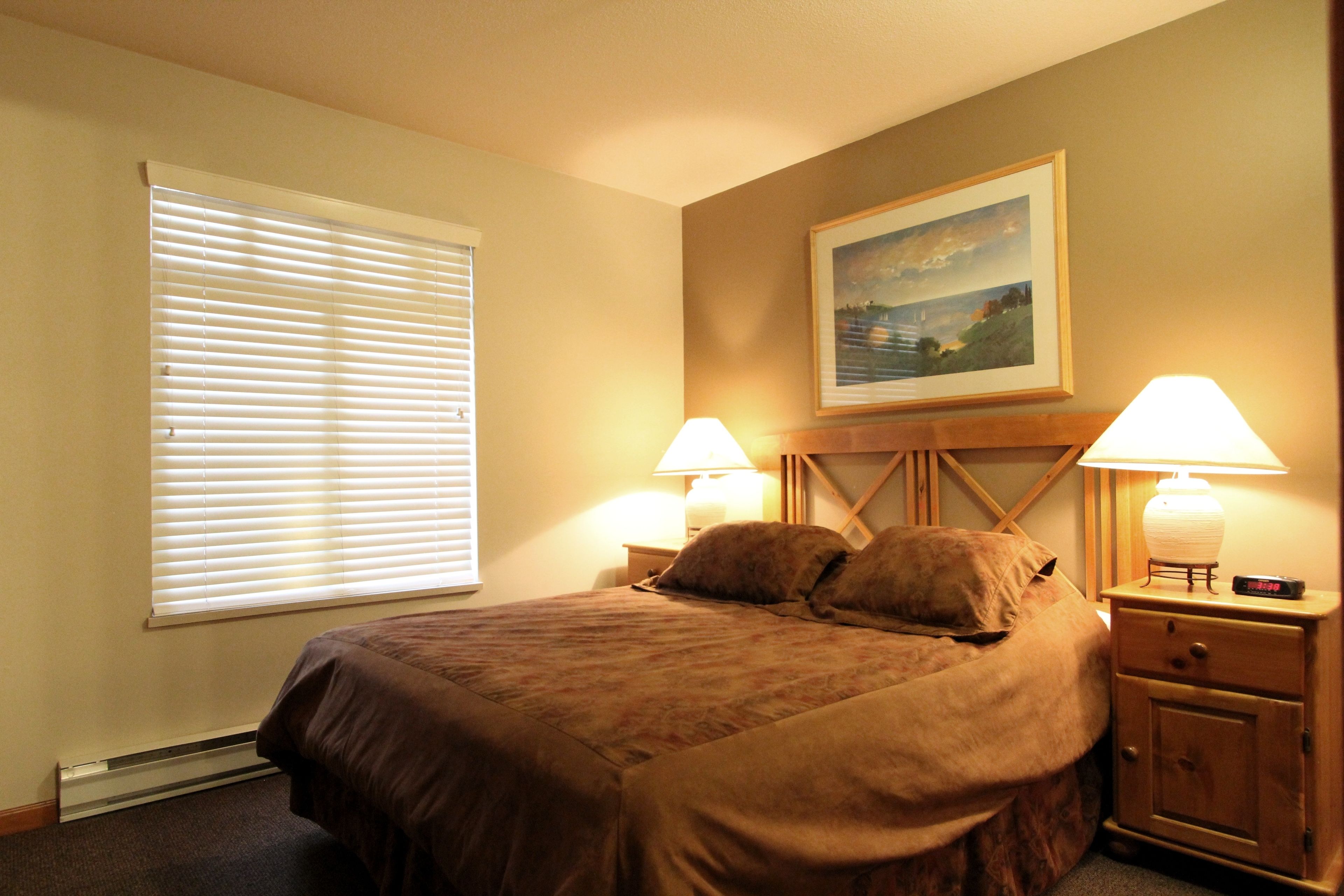 A bedroom with a large bed, two bedside lamps, a nightstand, and a painting on the wall.