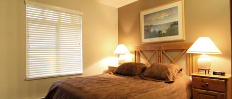 A bedroom with a large bed, two bedside lamps, a nightstand, and a painting on the wall.
