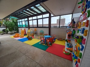 A children's play area with colorful mats, play structures, and a wall with alphabet letters.