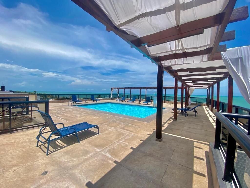 A rooftop pool area with lounge chairs, a swimming pool, and a view of the ocean.