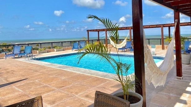 Zona de piscina con vista al océano, sillas de descanso y una hamaca.