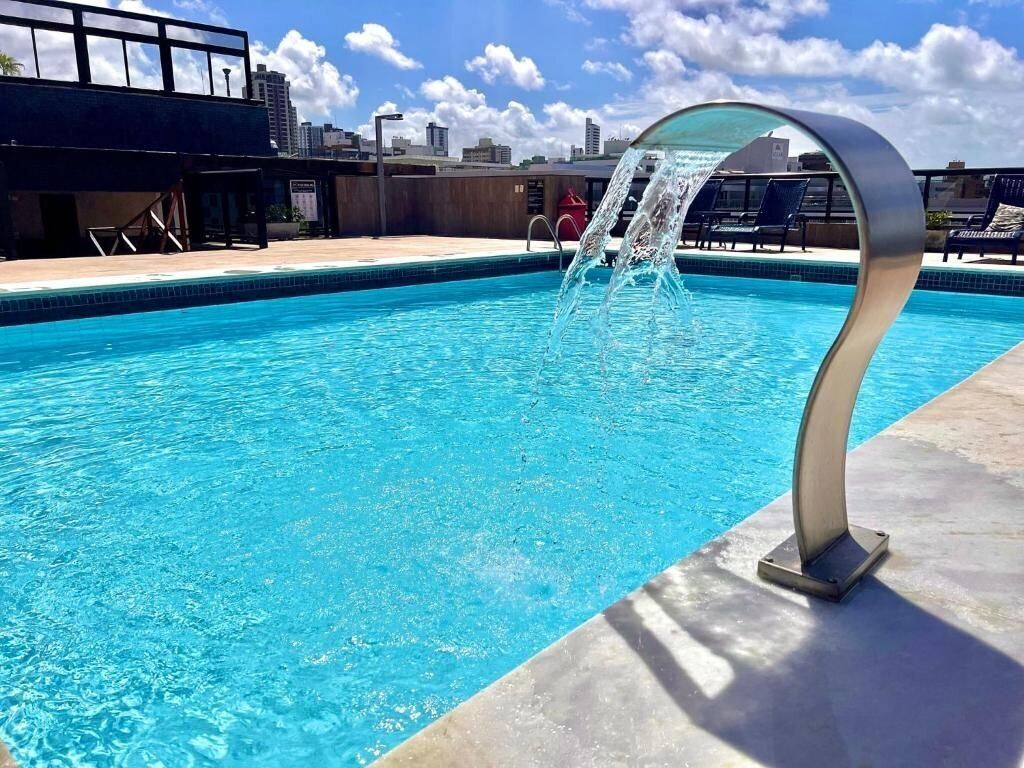 Una piscina con fuente, sillones de descanso y un paisaje urbano al fondo.