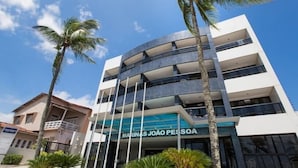 Un edificio de varios pisos con un diseño arquitectónico moderno, que cuenta con balcones y un cartel llamativo que dice 'MARINAS JOÃO PESSOA'.
