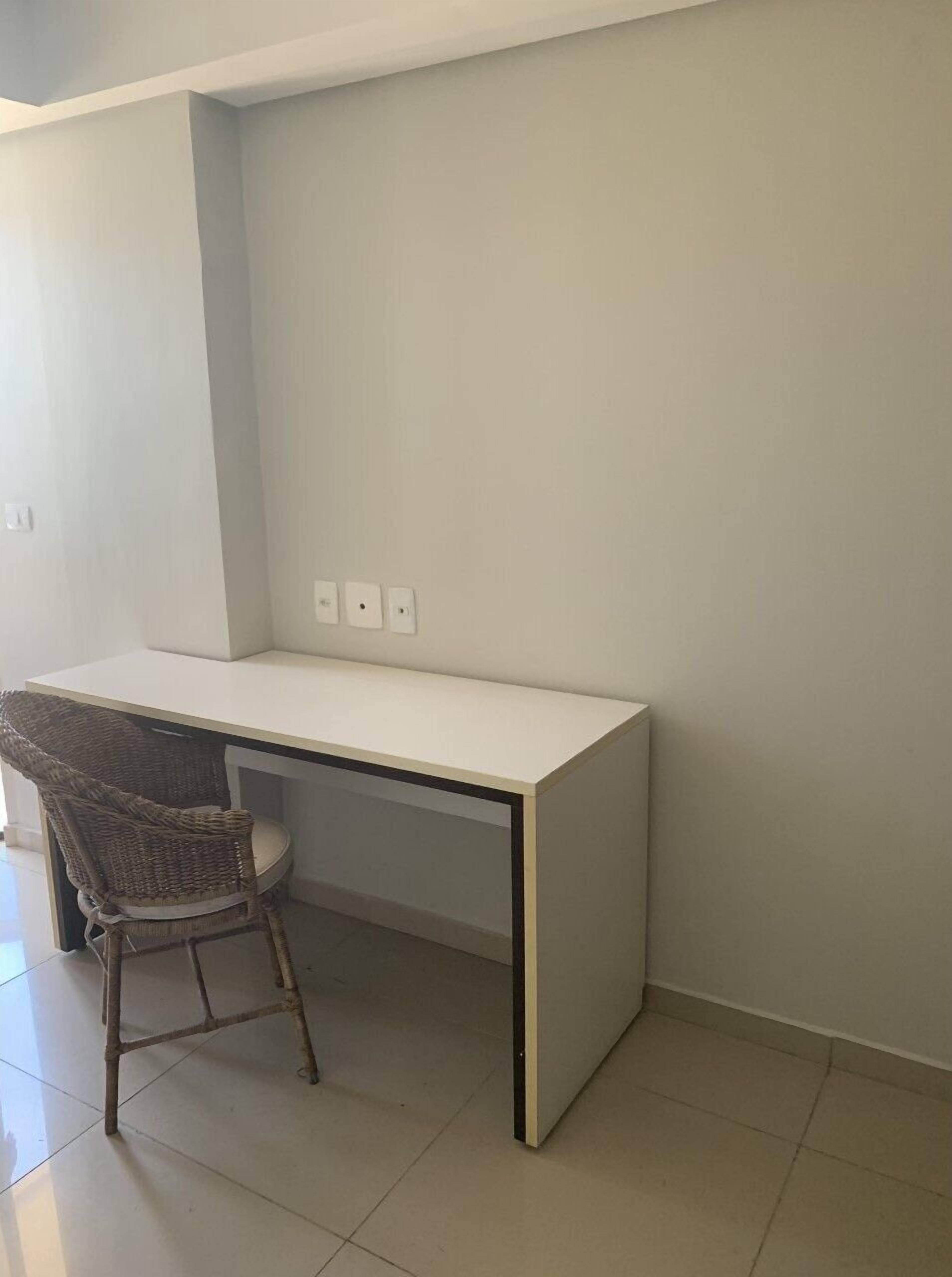 A room with a white desk, wicker chair, and a tiled floor.