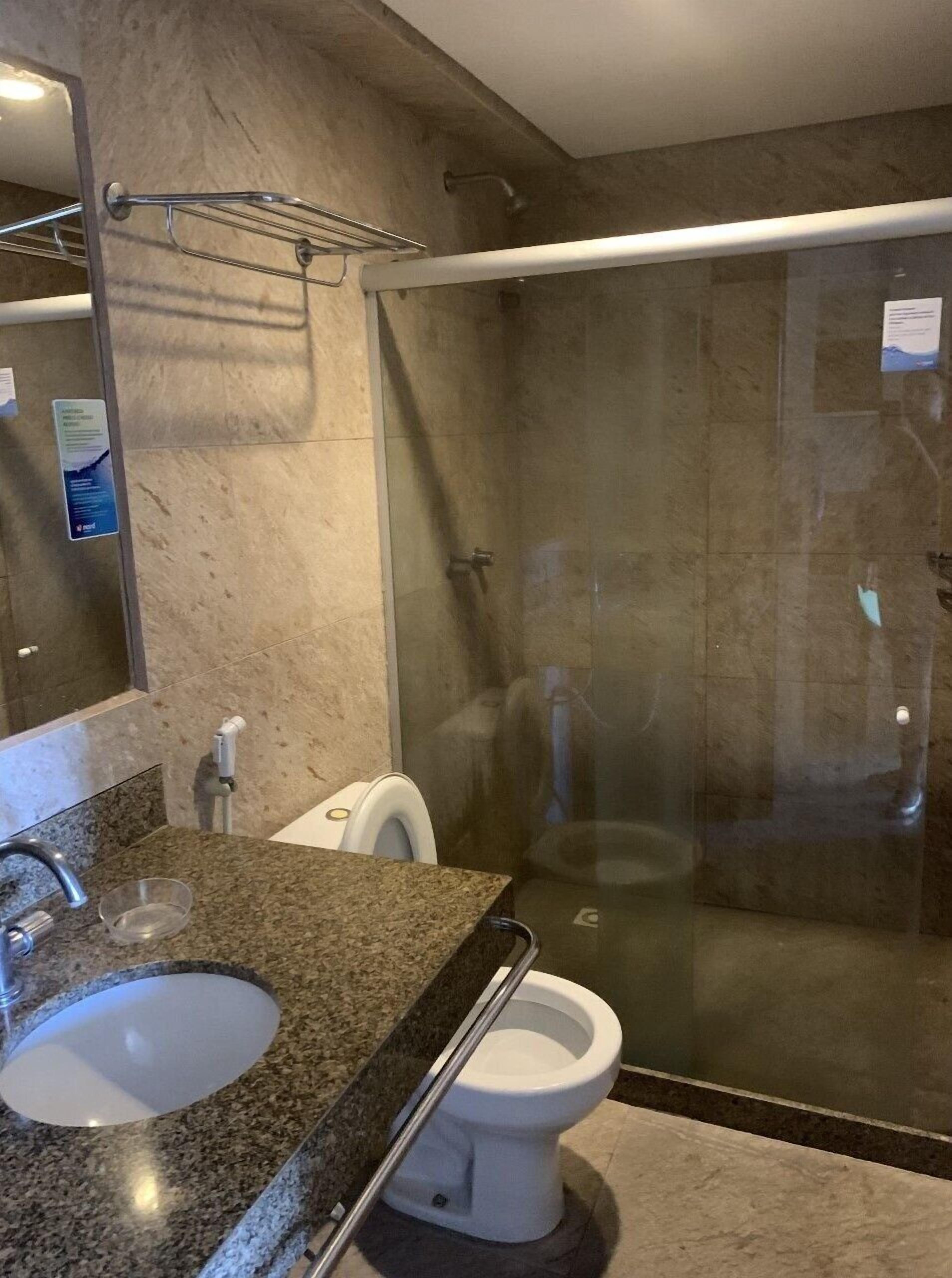 Un baño moderno con encimera de granito, inodoro blanco, ducha con mampara de vidrio y barra de toallas de metal.