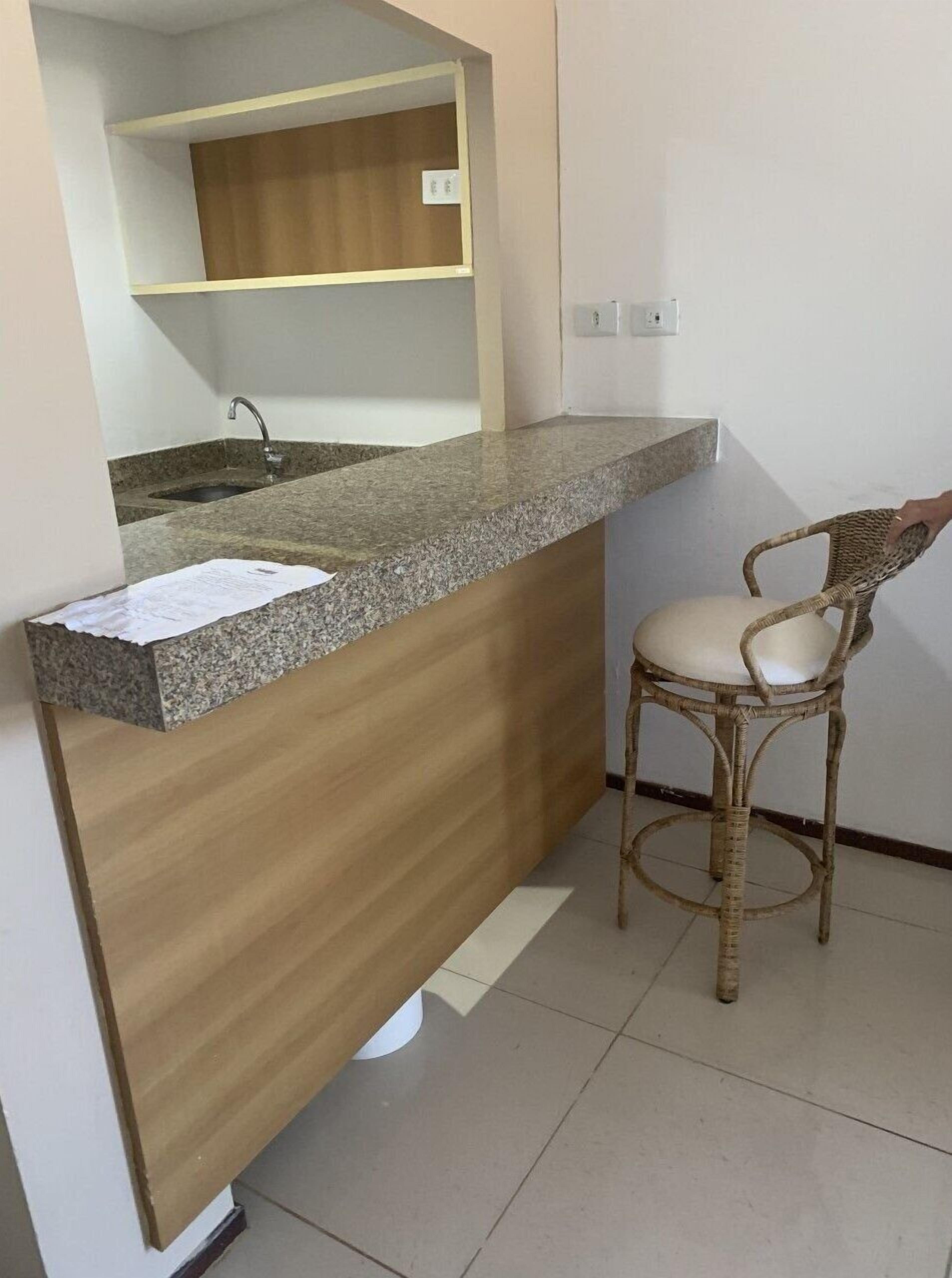 Cozinha com bancada de granito, armários de madeira, pia e cadeira de vime.