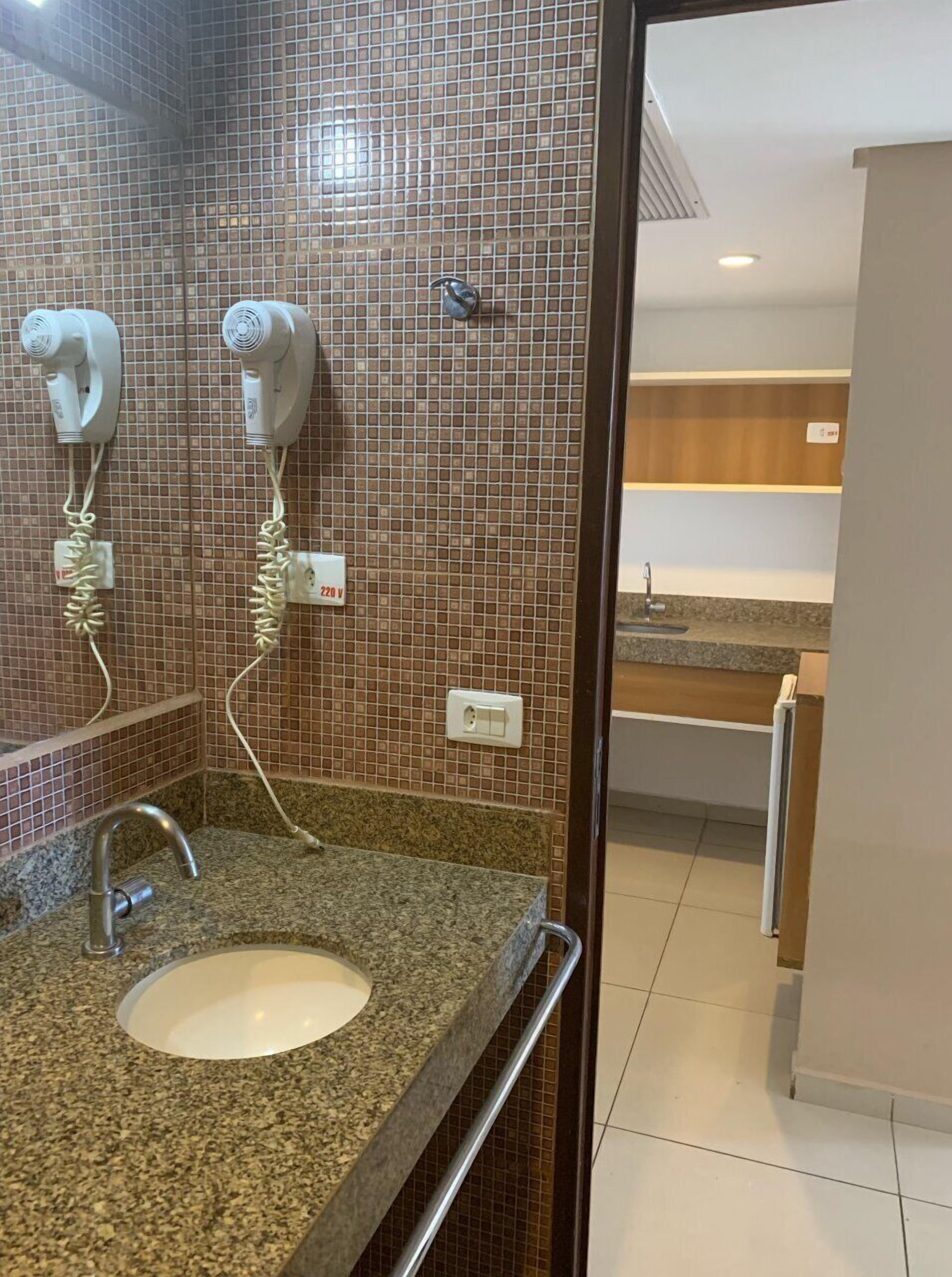 Un baño con encimera de granito, un lavamanos, un espejo, un perchero para toallas y zona de ducha.