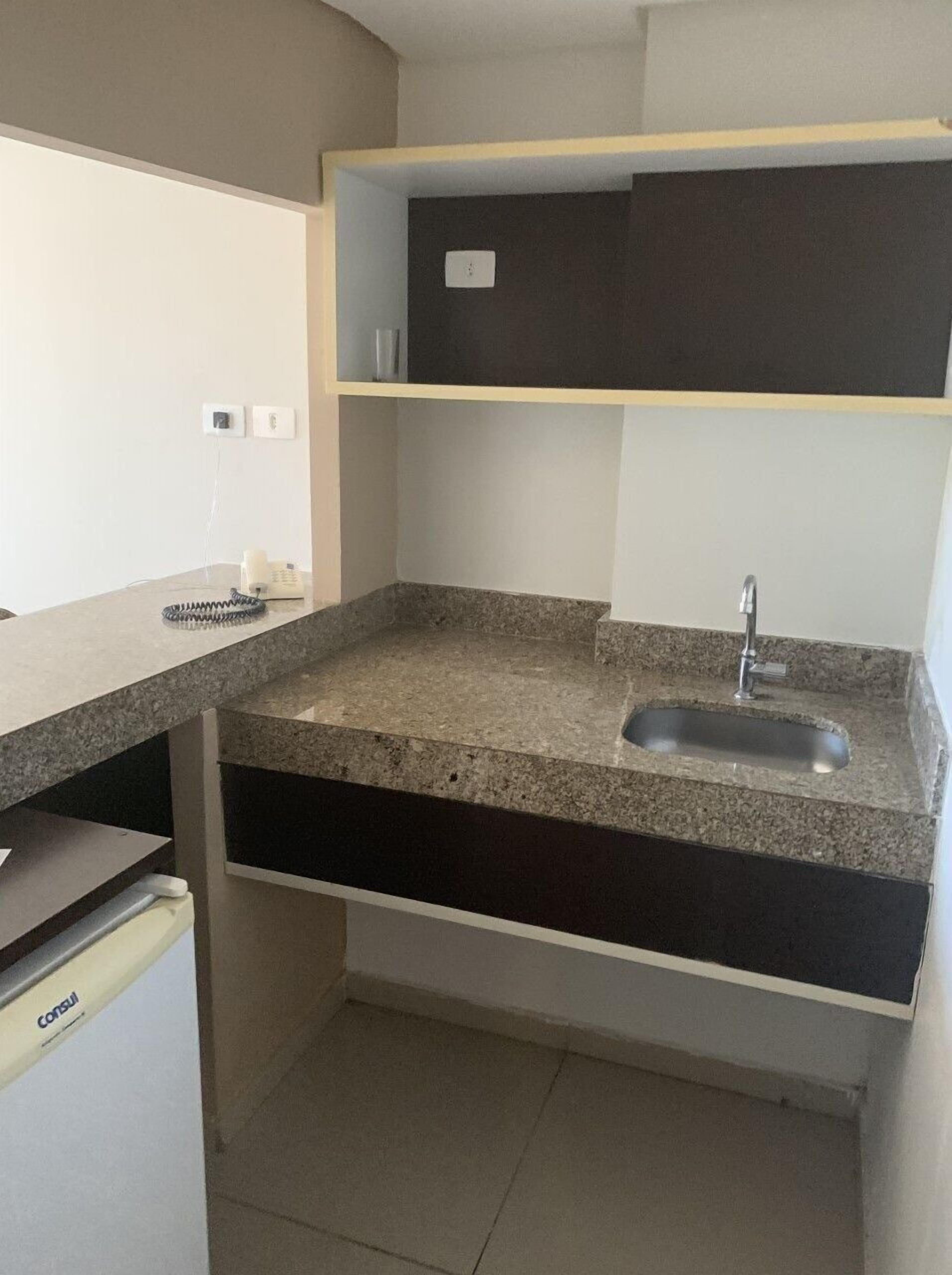 Eine kompakte Küche mit einer Granit-Arbeitsplatte, einem eingebauten Spülbecken und einem kleinen Kühlschrank.