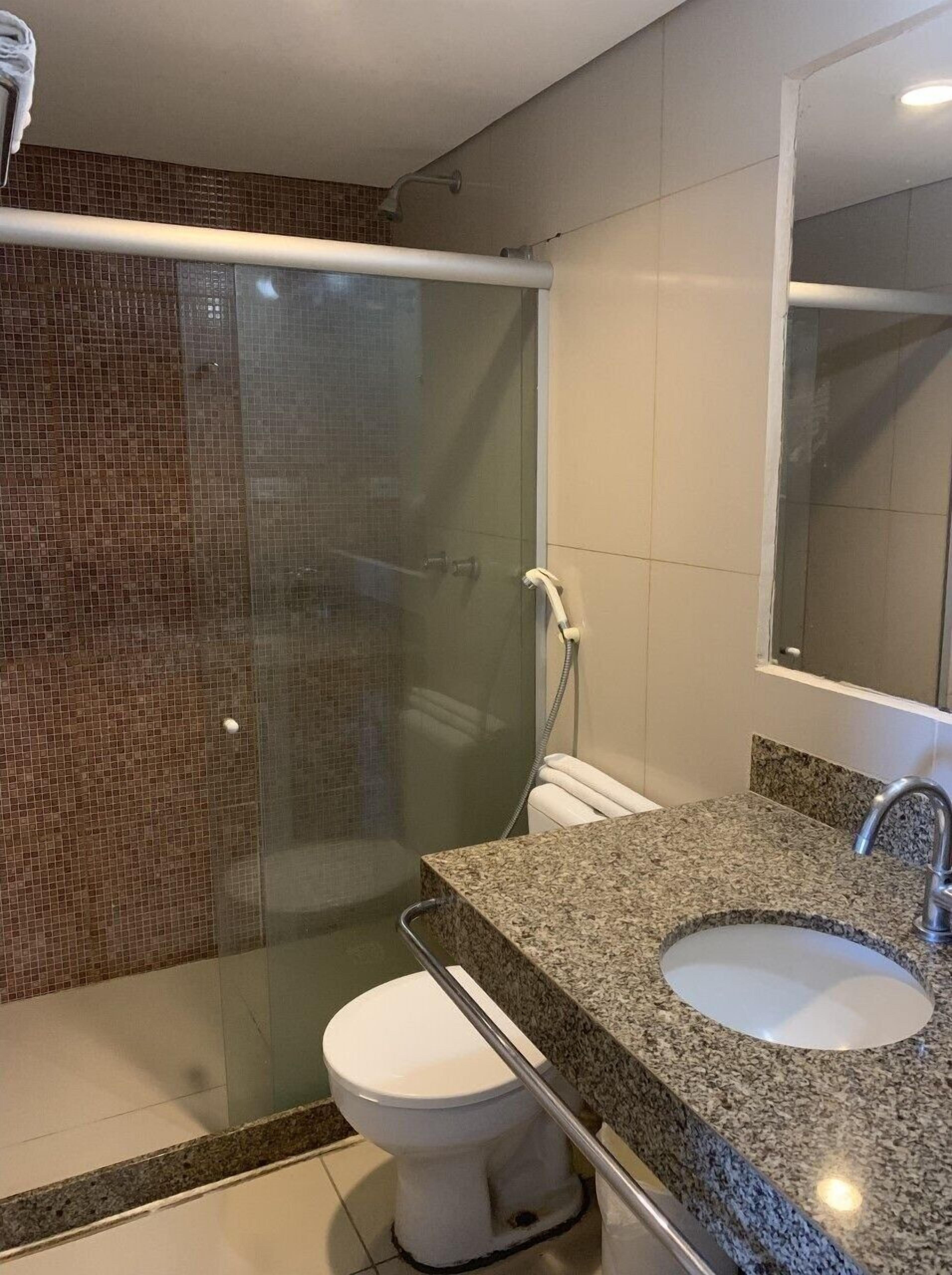 Un baño con cabina de ducha de vidrio, inodoro y encimera de granito con lavamanos.
