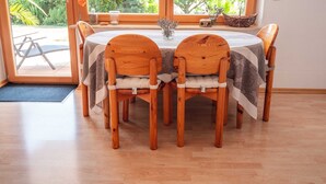 Zona pranzo con tavolo rotondo in legno e sedie, vista sulla vegetazione esterna e una finestra che si affaccia su alberi e un edificio.