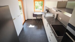 Una cucina compatta con piastrelle scure, forno integrato e finestra vista su del verde.