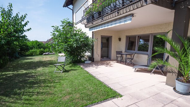 Un patio con prato, tavolo e sedie, e una pianta in vaso.