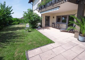 Une terrasse avec une pelouse, une table et des chaises, et un pot de fleurs.
