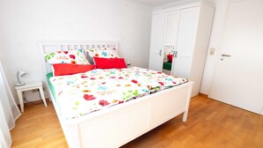 Una camera da letto con un letto bianco, biancheria da letto floreale, un comodino e un armadio.