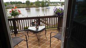 Un balcón con mesa y sillas, con vistas a un río con barcos y vegetación.