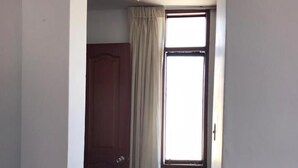 Un pasillo estrecho con piso estampado, una puerta de madera y una ventana con cortina.