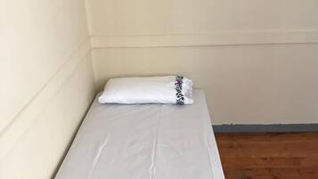 A small, single-bed room with a white mattress and a white pillow with a floral design.