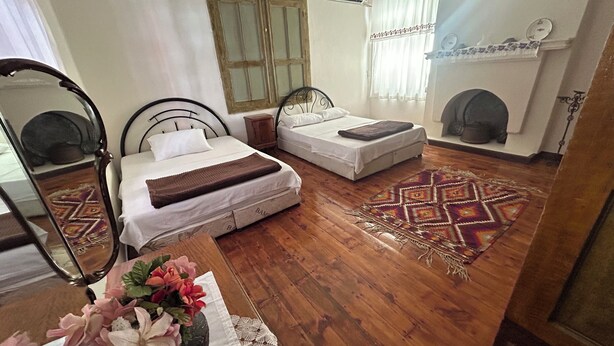 Un dormitorio con dos camas, piso de madera, alfombra estampada, chimenea y un espejo.