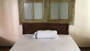 Uma cama com colchão e travesseiro brancos, um painel de cabeceira de madeira e uma janela com vidros jateados.