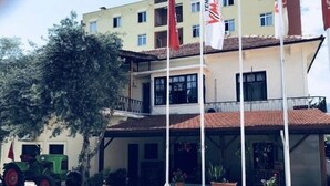 Un edificio de varios pisos con techo de tejas, un acceso cubierto y varias plantas en macetas.