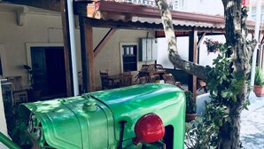Un tractor antiguo verde estacionado en un patio con zona de comedor y plantas en macetas.