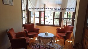 Una habitación acogedora con piso de madera, dos sillones rojos, una mesita redonda con mantel decorativo y un tapete estampado.