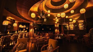 Un restaurant à la lumière tamisée, avec des meubles en osier et des lampes sphériques suspendues au plafond.