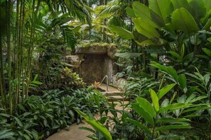 A lush indoor garden with a stone structure, various plants, and a pathway. - Royal Corin Thermal Water Spa and Resort (La Fortuna)