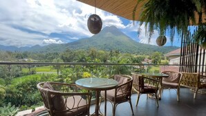 Un balcon agrémenté de meubles en osier et d’une table en verre, offrant une vue sur un paysage luxuriant avec une montagne en arrière-plan.