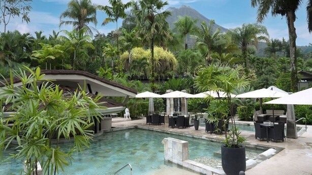 Un espace piscine doté de chaises longues et de parasols, entouré d’une végétation luxuriante et avec une montagne en toile de fond.