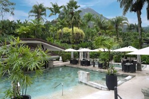 A pool area with lounge chairs and umbrellas, surrounded by lush greenery and a mountain in the background.