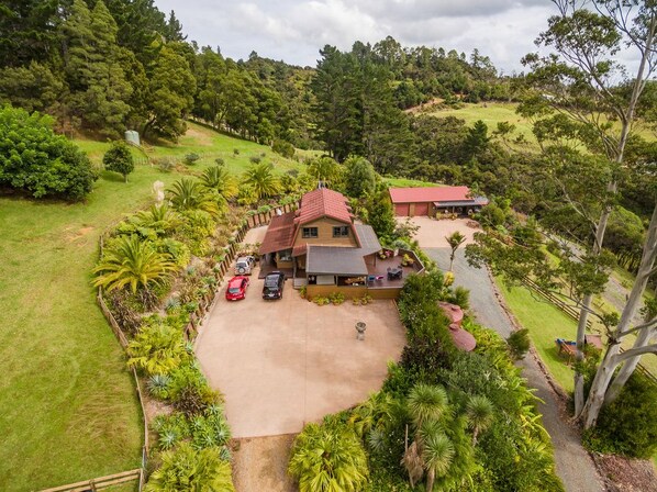 A house with a red roof, surrounded by lush greenery and a driveway.
