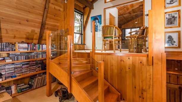 A wooden interior with a bookshelf, a staircase, and a chair.