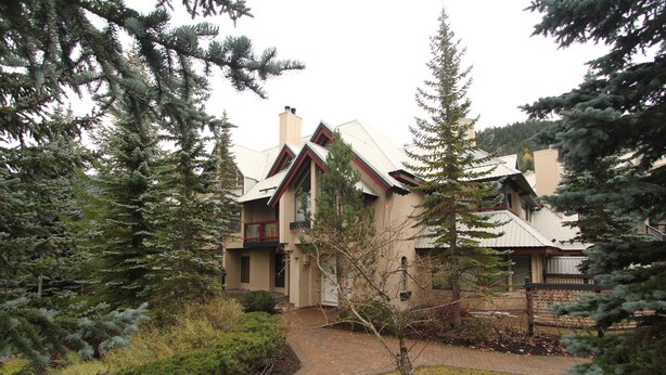 A two-story house with a brick pathway leading to the entrance, surrounded by dense evergreen trees. - Villas Snowberry by Whistler Retreats (Whistler)