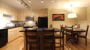 A modern kitchen with wooden cabinets, a microwave, a refrigerator, and a dining area with a table and chairs. - Villas Snowberry by Whistler Retreats (Whistler)