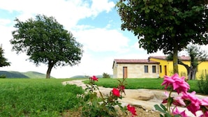 A yellow building with a red-tiled roof, surrounded by green fields and trees. - La Cerqua (Arcevia)