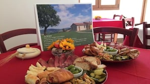 A table with a variety of food items including meats, vegetables, and bread, set against a red tablecloth in a dining area with wooden chairs and a framed picture of a landscape. - La Cerqua (Arcevia)