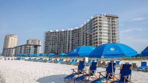 Um hotel na praia com vários andares, guarda-sóis azuis e cadeiras de praia.