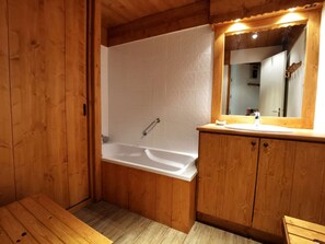 Un baño de madera con bañera, armarios de madera y un espejo.